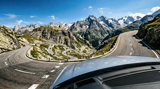 Steile Alpenpassstraße mit Serpentinen bei Sommerhitze, Fokus auf Motorhaube eines fahrenden Autos