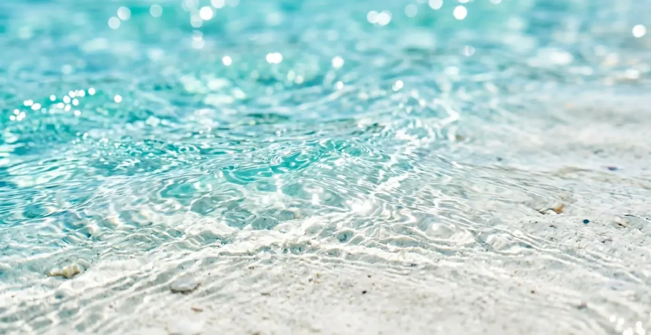 Nahaufnahme von kristallklarem türkisfarbenem Mittelmeerwasser mit sichtbarem weissen Sandboden in geringer Tiefe