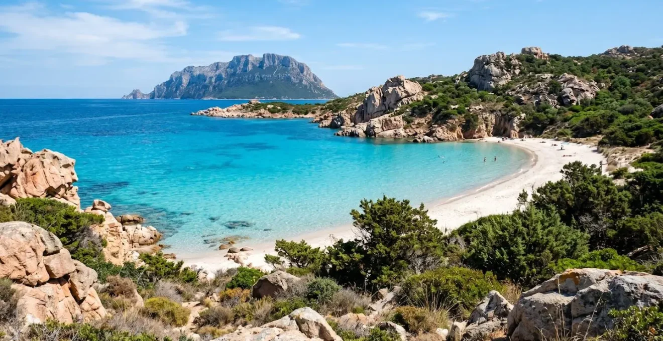 Weitläufige sardische Küstenbucht mit türkisfarbenem Wasser, weißem Sandstrand und Granitfelsen unter strahlendem Mittelmeerhimmel