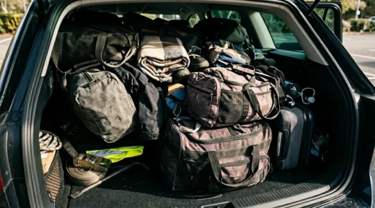 Warnweste im vollgepackten Kofferraum tief unter Gepäck versteckt - Symbol für gefährliche Unzugänglichkeit bei Notfällen